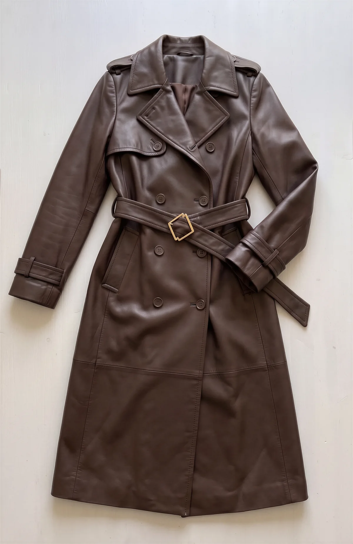 Product photo: a brown leather trench coat laid flat, with its belt buckled