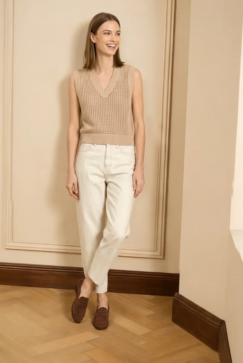 Look 5: the model leaning on the wall in the crochet vest and ecru jeans, laughing