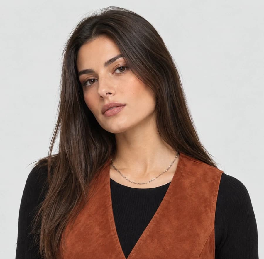 Studio photo of a model in a rust suede vest with smooth, airbrushed, overly polished skin