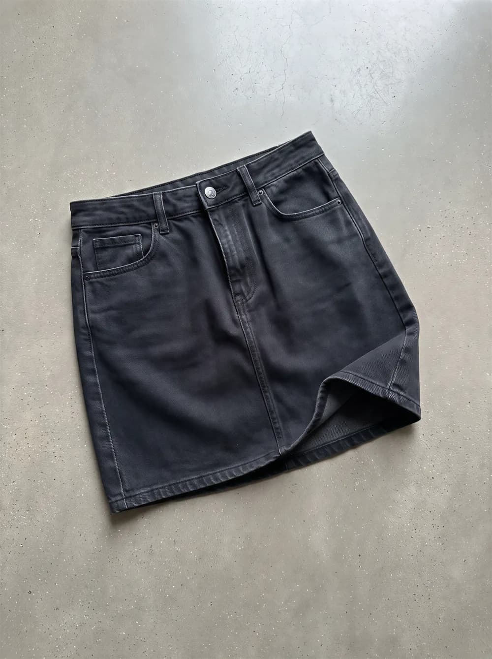 Product photo: a black denim mini skirt laid flat on concrete