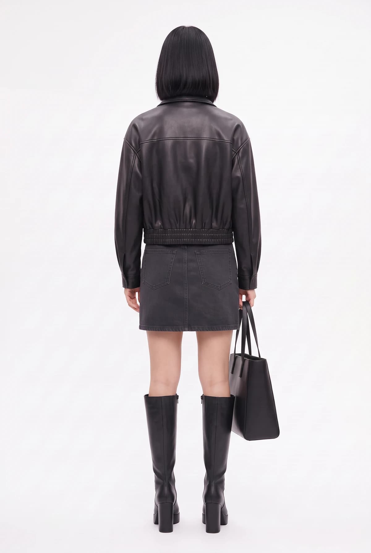 The same outfit from the back: leather jacket, black skirt, boots, and tote bag