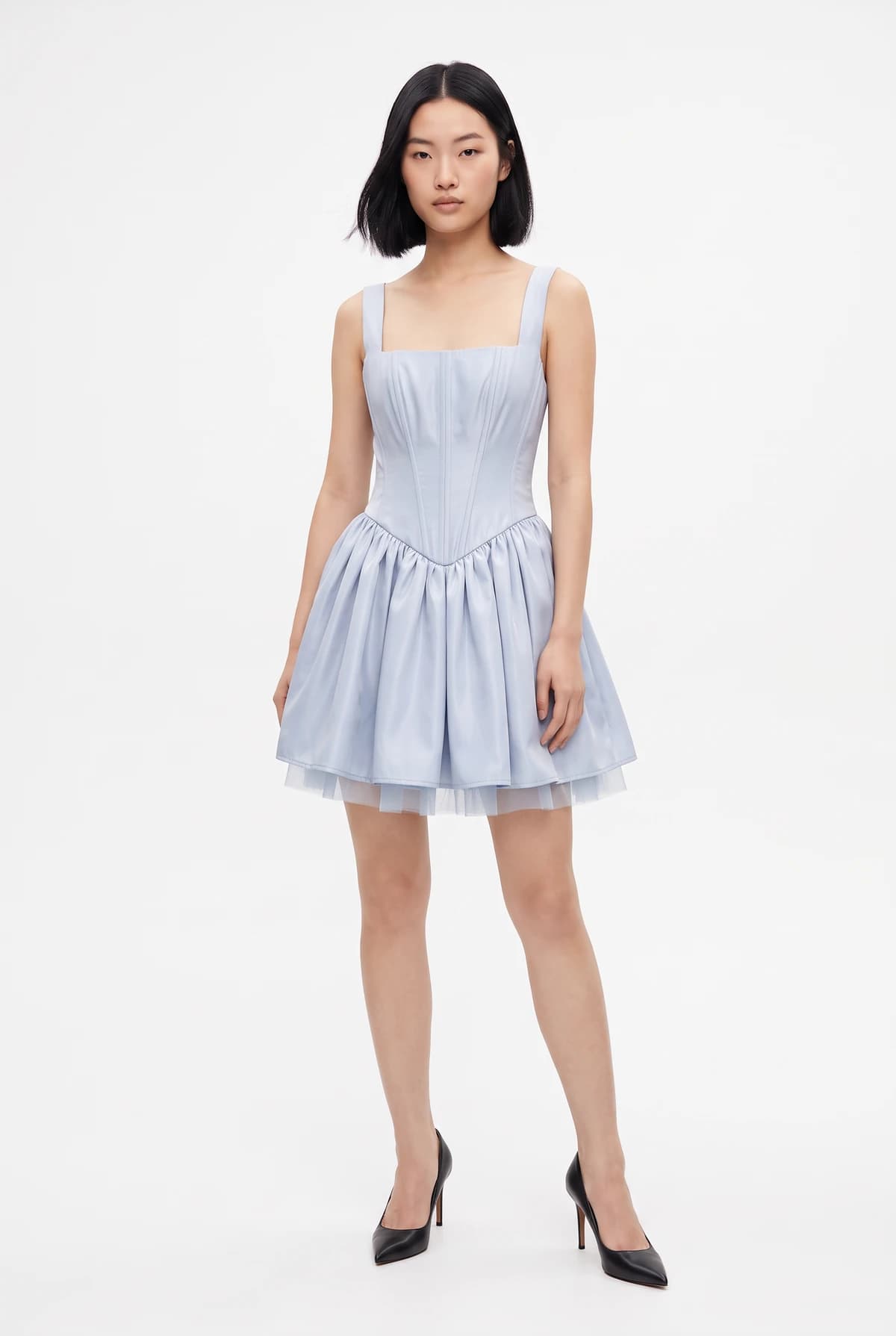 The same model now wearing the light blue corset dress, with her pose, heels, and background unchanged